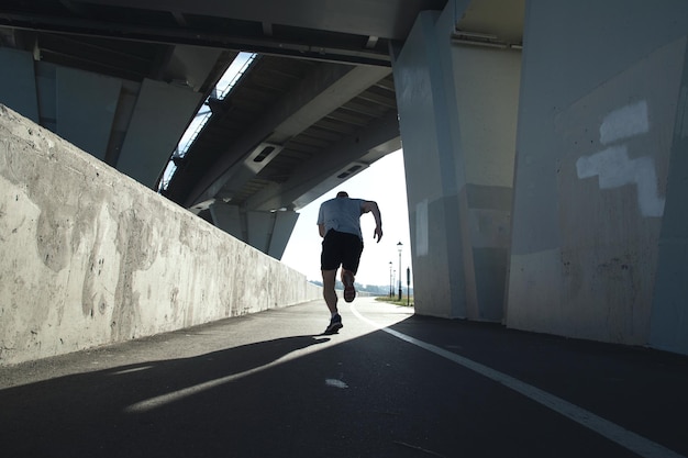 Rear view of a running sportsman under a bridge