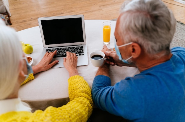 Photo rear view of senior couple using laptop while having cup of coffee at home