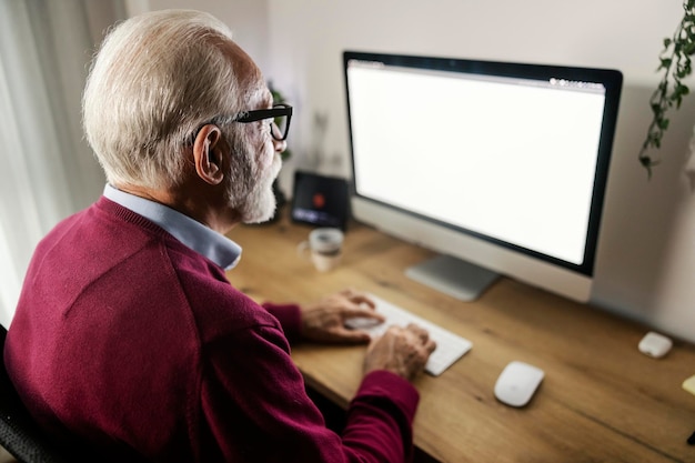 Photo rear view of a senior entrepreneur sitting at home office and typing on keyboard