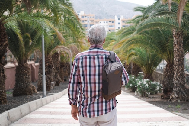 여행과 휴가를 즐기는 테네리페의 거리를 걷고 있는 배낭을 메고 있는 고위 관광 남성의 뒷모습