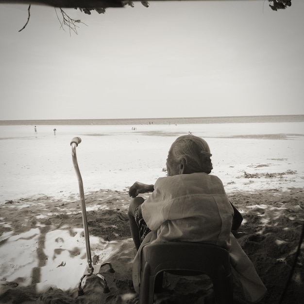 Foto vista posteriore di una donna anziana seduta sulla spiaggia