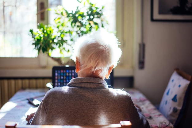 Foto vista posteriore di una donna anziana che usa un portatile mentre è seduta a casa