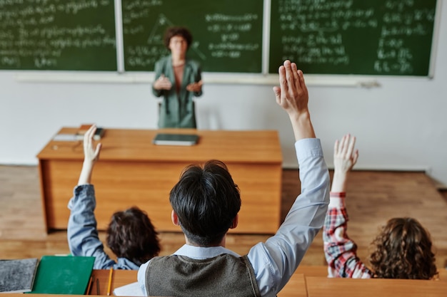 Rear view of several youthful students keeping their hands raised at lesson