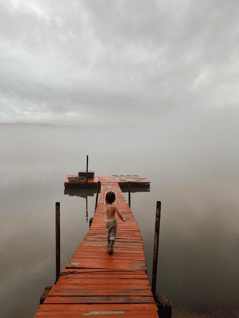 Rear view of shirtless boy walking on pier in lake