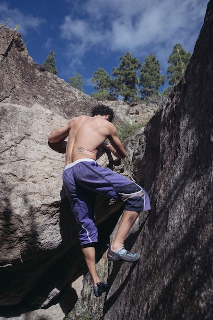 Foto vista posteriore di un uomo senza camicia che si arrampica sulla roccia contro il cielo