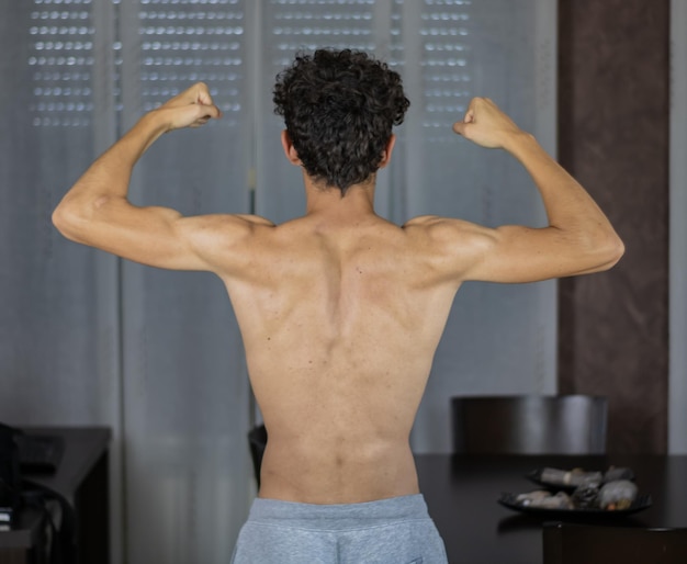 Photo rear view of shirtless man flexing muscles at home