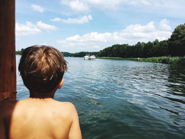 Rear view of shirtless man looking at sea against sky