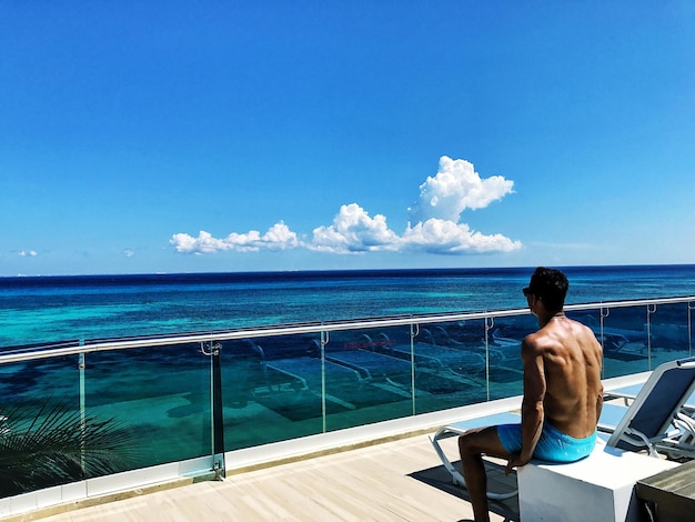 Photo rear view of shirtless man looking at sea on sunny day