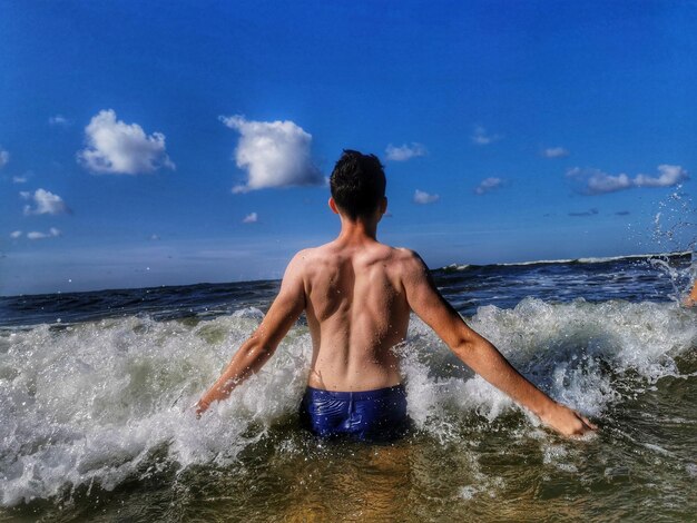 Rear view of shirtless man in sea against sky