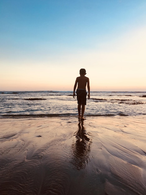 Rear view of shirtless man standing on beach during sunset