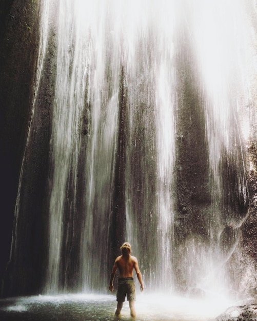 rear view of shirtless man standing at waterfall