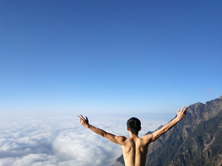 Photo 青い空に逆らって腕を伸ばしたシャツのない男の後ろの景色