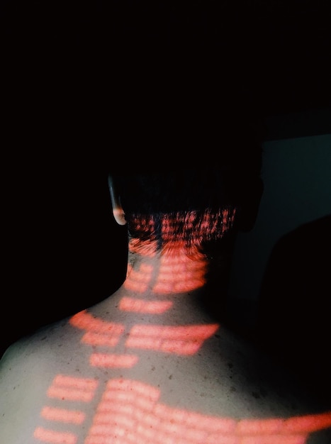 Photo rear view of shirtless man with red lights against black background