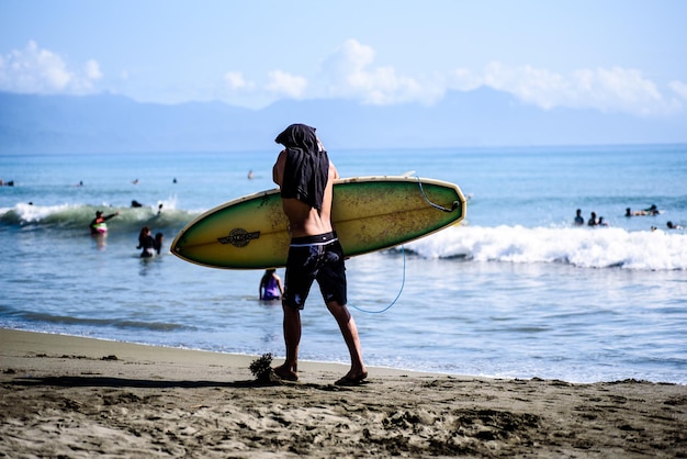 rear view of shirtless man with surfboard walking at beach