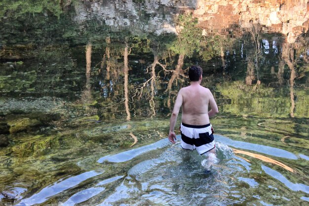 Photo rear view of shirtless mature man standing in lake at forest