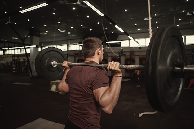 Rear view shot of male athlete working out with heavy barbell at cross fit gym