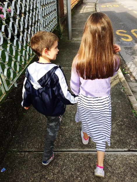 Photo rear view of siblings walking on footpath