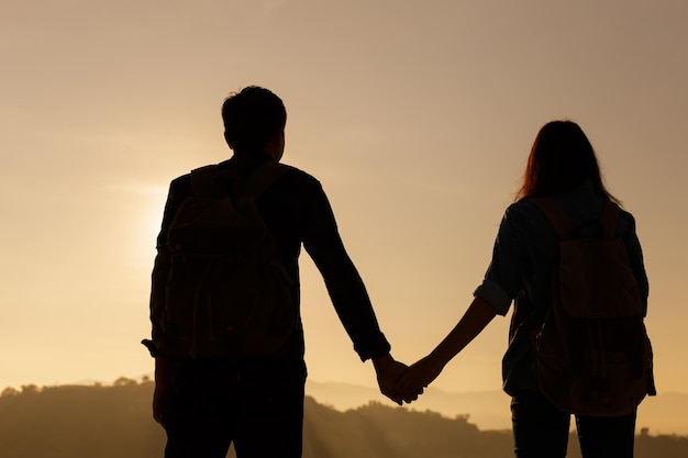 rear view of silhouette couple holding hands while standing against orange sky during sunset