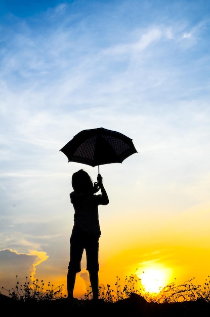 Photo rear view of silhouette girl holding umbrella against sky during sunset