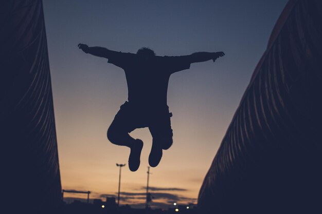 夕暮れの空に向かってジャンプするシルエット男の後ろの景色