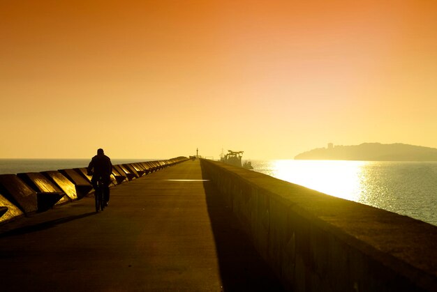 Rear view of silhouette man riding bicycle on pier