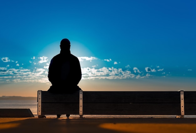 Rear view of silhouette man sitting against sea at sunset