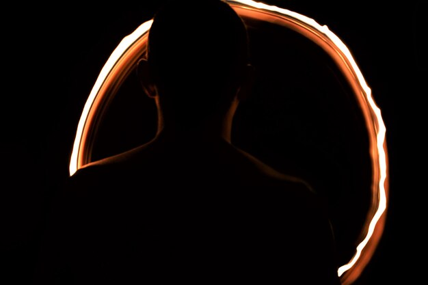 Photo rear view of silhouette man spinning fire in circle shape at night