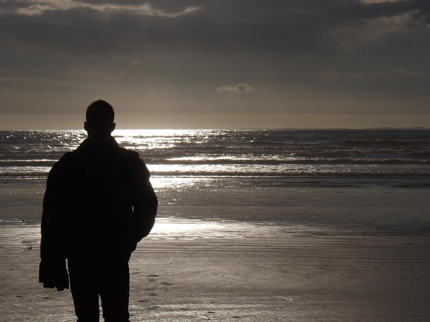 Foto vista posteriore di un uomo in silhouette in piedi sulla spiaggia
