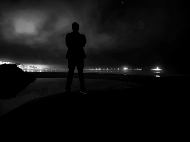 Rear view of silhouette man standing on illuminated street light