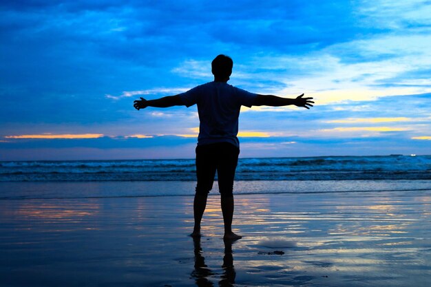 Rear view of silhouette man standing at sea shore against sky