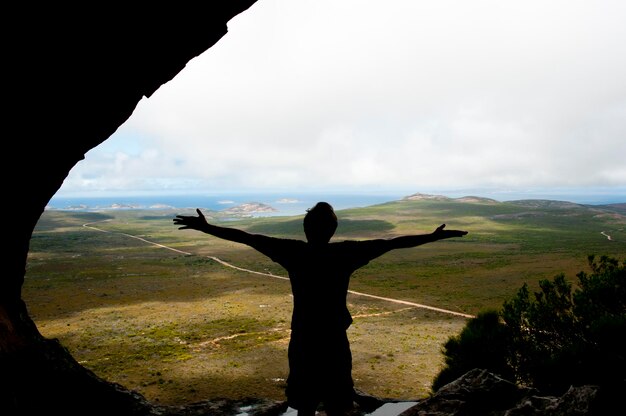 Задний вид силуэта человека с вытянутыми руками, стоящего в пещере напротив неба