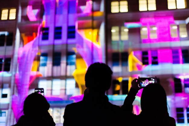 Photo rear view of silhouette people photographing illuminated building at night