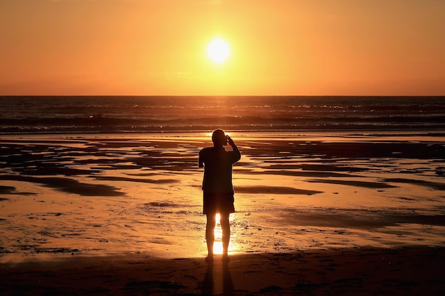 Foto silhouette di vista posteriore di una donna single takong foto del tramonto in piedi su una spiaggia