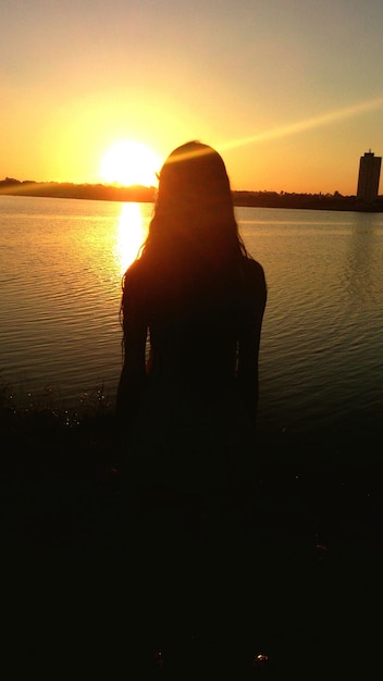 Задний вид силуэта женщины на фоне озера во время захода солнца