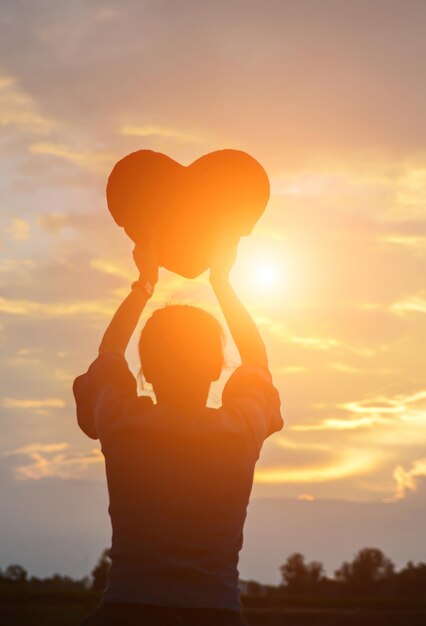 Foto vista posteriore di una donna a silhouette in forma di cuore contro il cielo arancione durante il tramonto