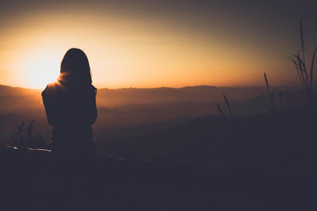 Rear view of silhouette woman standing against sky during sunset