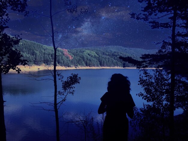 Foto vista posteriore di una silhouette di donna in piedi vicino al lago di notte