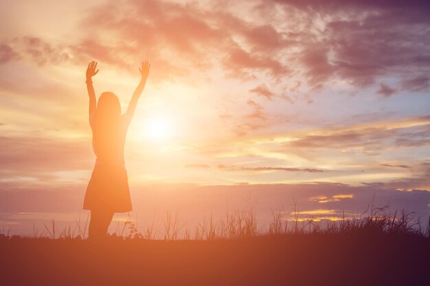 Rear view of silhouette woman with arms raised standing on land against sky during sunset