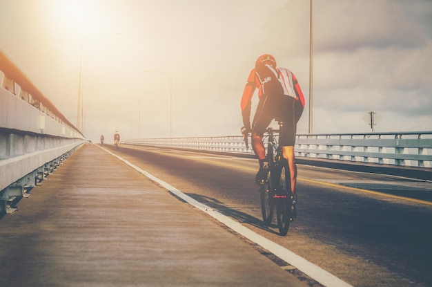 Rear view of sportsman riding bicycle on bridge against sky