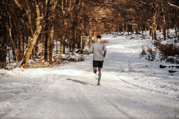 Rear view of sportsman running in nature on snow at winter. Winter fitness, fitness in nature, chilly weather