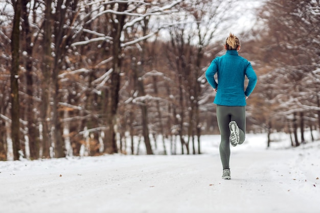 雪の降る天気で自然の中でジョギングするスポーツ選手の背面図。