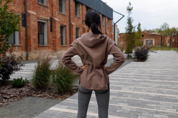 Rear view of sporty woman holding hands on waist outdoors