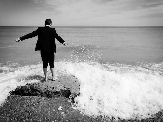 Rear view of teenage boy standing against sea at beach