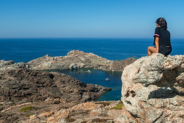 Rear view of a teenage girl sitting on the rocks of the cap de creus headland in catalonia spain