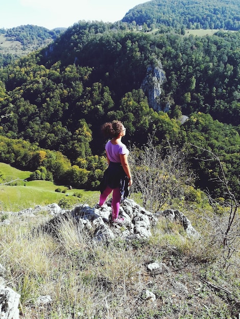 山の上に立っている十代の女の子の後ろの景色