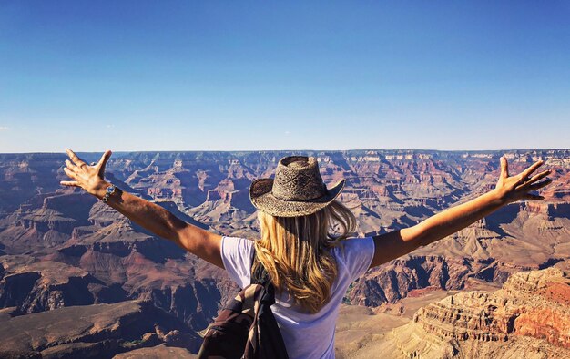 Foto vista posteriore di una ragazza adolescente con le braccia tese in piedi sulla montagna contro un cielo blu limpido