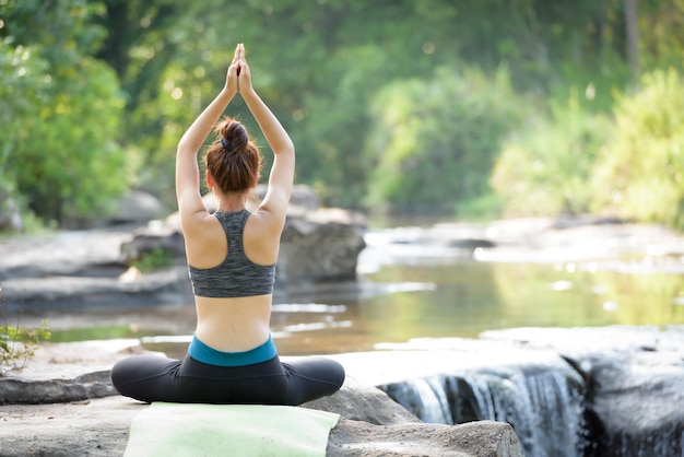 Rear view of teenage girl with arms raised exercising on rock formation