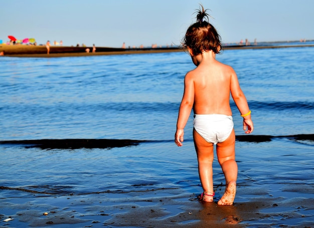 Photo rear view of toddler standing at beach