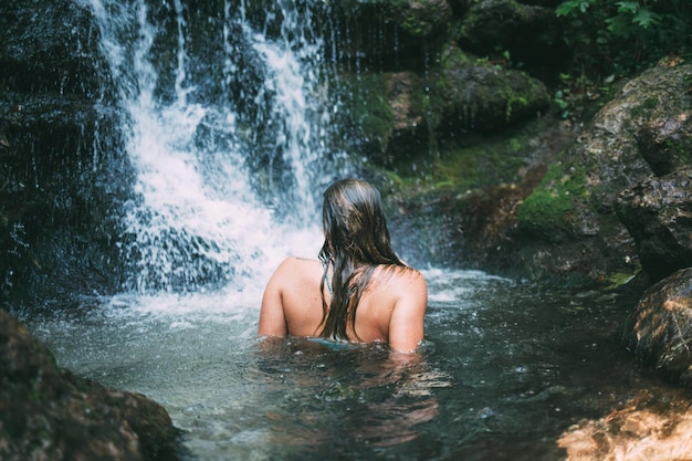 Foto vista posteriore di una donna in topless che si gode una cascata nella foresta