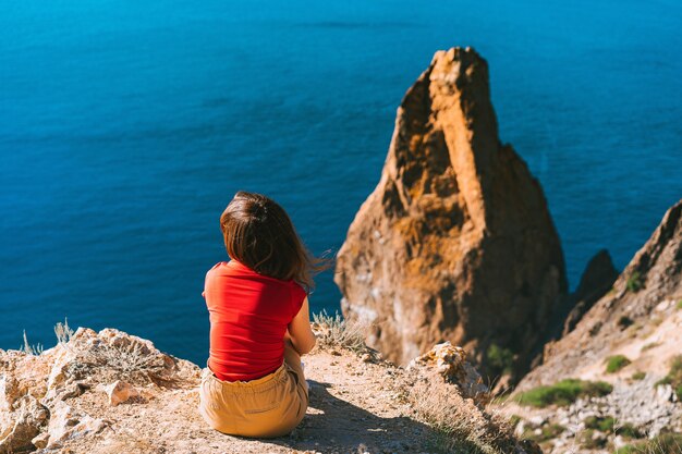 Vista posteriore della donna del viaggiatore in piedi sul bordo della scogliera davanti al fantastico paesaggio marino, concetto di viaggio.